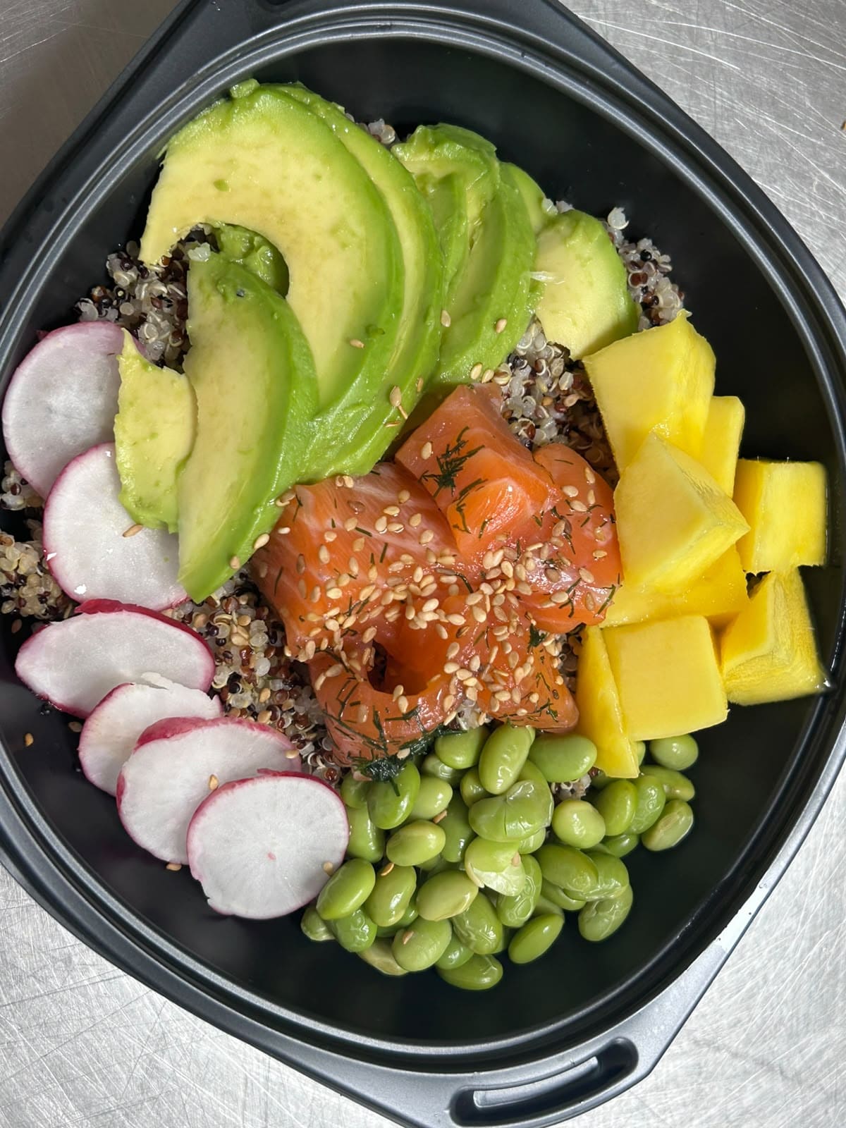 Barquette noire garnie de quinoa, saumon, avocat, edamame, radis et dés de mangue